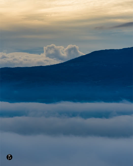 Paesaggio montano con nuvole basse e cielo al tramonto.