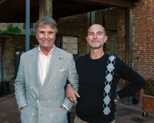 Due uomini in posa all'aperto, uno con giacca grigia e l'altro con maglione nero con motivo a rombi. Sullo sfondo, un edificio in mattoni. Uno degli uomini è Brunello Cucinelli, l'altro Paolo Zuchegna Fotografo Umbria Toscana Ritratti Immobili Aziende, Google Street View e opere d'arte. Perugia, Città della Pieve, Orvieto.