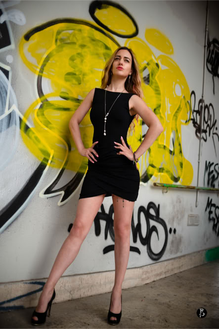 Donna in abito nero posa davanti a un muro con graffiti gialli e neri.