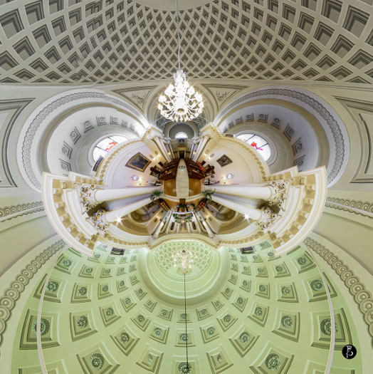 Vista distorta di un soffitto a cupola con dettagli architettonici intricati e un lampadario centrale.