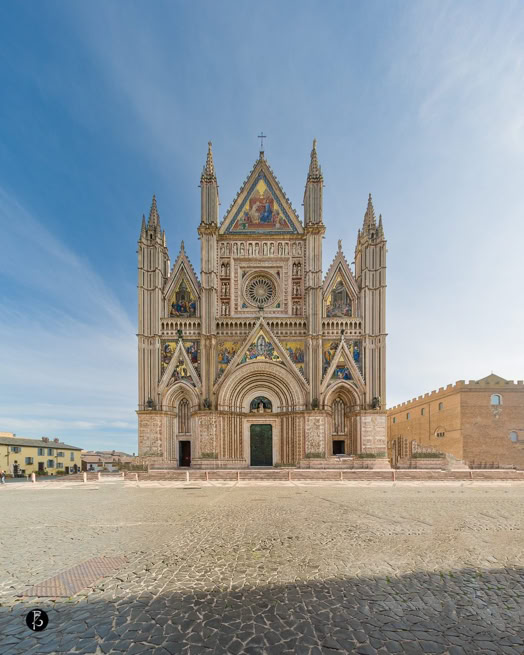 Facciata di una cattedrale gotica con dettagli decorativi e pinnacoli, situata in una piazza pavimentata.
