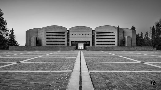 Edificio moderno con facciata curva e linee orizzontali, visto da una piazza pavimentata con motivo geometrico.