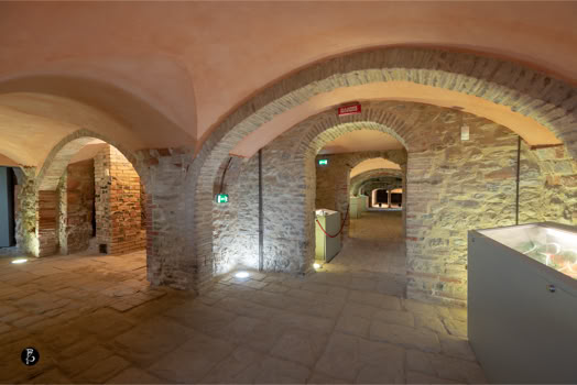 Interno di un edificio con archi in pietra, illuminazione soffusa e pavimento in pietra.