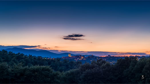 Panorama di un paesaggio al tramonto con colline, alberi e un cielo blu scuro con una nuvola.