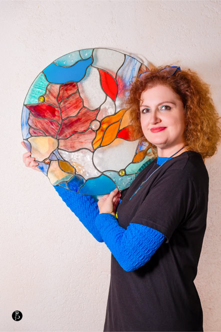 Donna con capelli ricci rossi tiene un pannello rotondo di vetro colorato con motivi astratti.