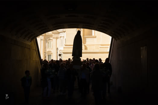 Persone camminano attraverso un tunnel verso una statua illuminata dalla luce del giorno.