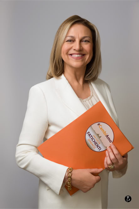 Donna sorridente in abito bianco che tiene una cartella arancione.