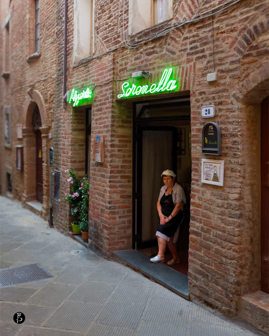 Edificio in mattoni con insegna al neon verde sopra l'ingresso, una persona in piedi sulla soglia.