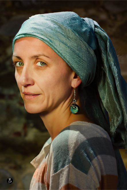 Donna con un foulard azzurro in testa, indossa un maglione a righe e orecchini pendenti, sfondo sfocato.