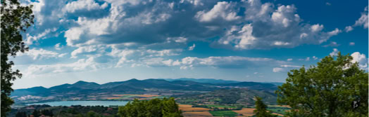 Paesaggio con lago, colline, alberi e cielo nuvoloso.