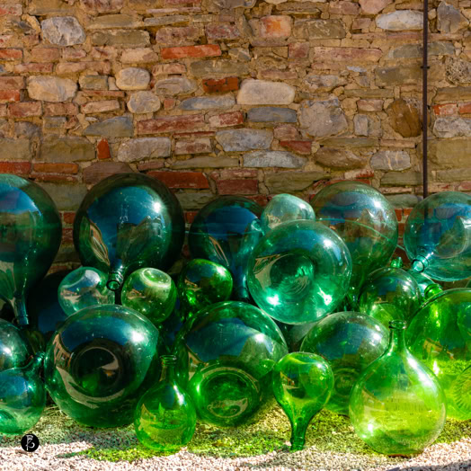 Sfere di vetro verdi e blu disposte davanti a un muro di pietra.