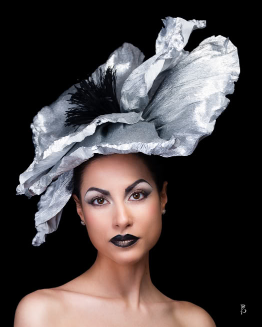 Donna con cappello argentato di grandi dimensioni su sfondo nero.