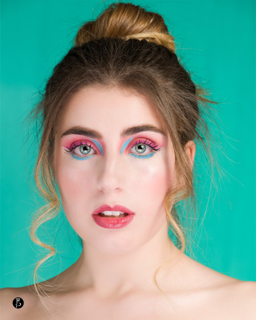Donna con trucco colorato e capelli raccolti, su sfondo verde.