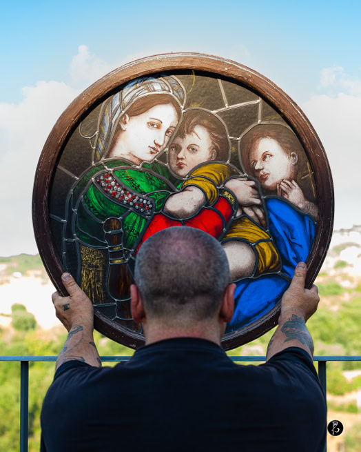 Uomo di spalle tiene un vetro rotondo colorato con l'immagine di tre figure.