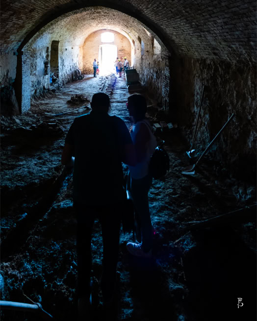 Due persone camminano in un tunnel buio con un'apertura luminosa in fondo.